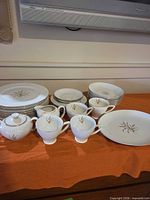 Complete dinnerware set stacked on surface showing plates, bowls, cups, sugar, creamer, platter