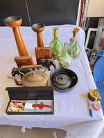 All items grouped on table: glass bottles, cast-iron teapot in trivet, copper kettle, wooden candlesticks, elephant bookends, knife box
