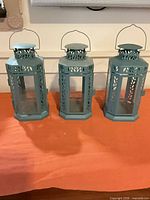 Front view of three teal metal and glass lanterns standing side-by-side