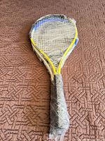 Full view of racket wrapped in plastic showing yellow frame and worn strings