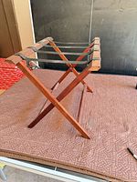 Side view of folded-out wooden luggage rack showing X-frame and fabric straps