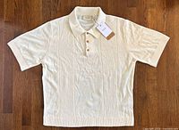 Full view of front of cream knit polo shirt laid flat