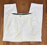 Full view of off-white pleated cotton pants laid flat