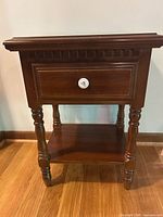 Front view of nightstand showing drawer, knob, turned legs, shelf