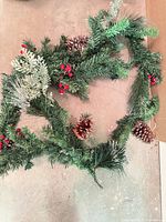 Artificial evergreen garland with pinecones and red berry picks lying on floor