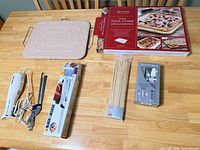 All four items laid out: electric knife with box, pizza stone with box, bamboo skewers, cutlery set