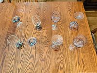 Eight stemmed glasses viewed from above on wooden table showing mix of plain and decorated pieces