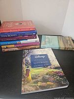 Stack of six books including Disney Thomas Kinkade coloring book front cover visible