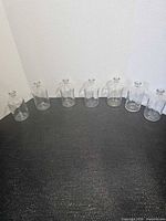 Seven clear glass apothecary bottles lined in a row on black surface