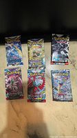 Front view of six sealed Pokemon booster packs from various sets laid flat