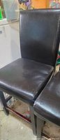 Two black faux leather dining chairs showing seats, backs, and wood legs