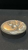 Closed oval pewter box showing floral relief lid