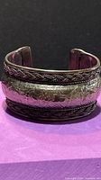 Front view of wide silvertone cuff showing embossed floral panel and braided borders
