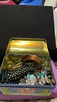 open tin showing assorted vintage jewellery pieces