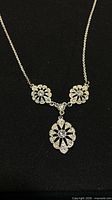Full view of necklace on black background showing chain and three floral crystal medallions