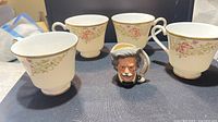 Front view of four teacups and character jug