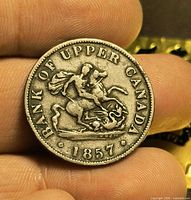 Obverse of 1857 Bank of Upper Canada token held between fingers, clear legend and date visible