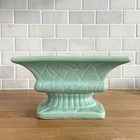 Front view of aqua stoneware pedestal planter showing leaf pattern and flared rim
