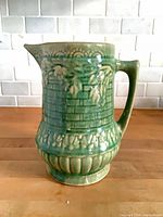 Front view of green ceramic pitcher showing basketweave and rose relief
