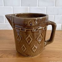 Side view of brown stoneware pitcher showing relief diamond pattern, spout and handle