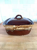 Front angled view of brown drip glazed square casserole with lid on wooden surface