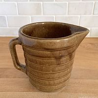 Front view of mocha brown ribbed stoneware pitcher showing handle and spout