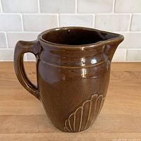 Front three-quarter view of brown stoneware pitcher showing handle, spout and Gothic arch motif