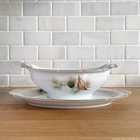 Side view of sauce boat on underplate displaying pine cone design and gold trim