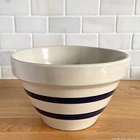 Angled view of cream stoneware mixing bowl showing two cobalt stripes, rolled rim and tapered profile