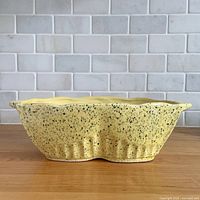 Side view showing yellow speckled glaze, ribbed base and scalloped rim