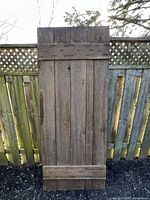Full view of vertical-slat pine door leaning against fence