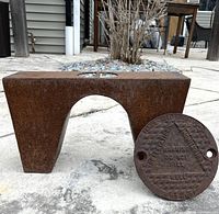 Both rusted steel pieces together—arched block and round well cover