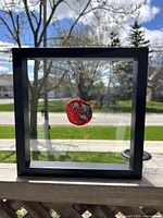 Front view of framed fused glass art showing red disk on clear glass