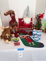 Group image showing all Christmas decorations on table including plush reindeer, gnome, bench, tree, stocking, ribbon, garlands, jingle bells and timer boxes