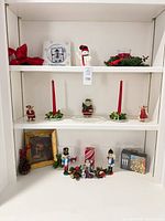 Overview of shelf displaying nutcrackers, figurines, candles, framed nativity print, boxed plates and string lights