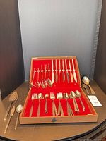 Open fitted box showing majority of flatware pieces and separate serving pieces laid out