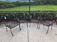 Four black wrought iron patio chairs arranged around patio fence