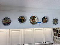 All five hand-painted ceramic wall plates displayed on wall