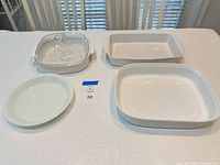 Four white baking dishes including covered casserole, rectangular pan, square casserole, round plate