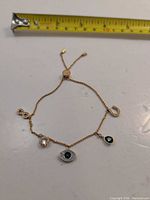 Full view of gold-tone adjustable charm bracelet showing all charms and tape measure for scale