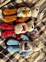 Three state-themed plush bears laid out on bed showing fronts and tags