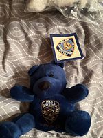 Front view of navy NYPD plush teddy bear showing embroidered badge and attached tag