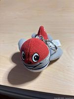 Front view of red and gray plush airplane keychain showing face and keyring