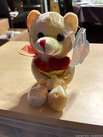 Front view of tan teddy bear holding red hearts with hang tag visible