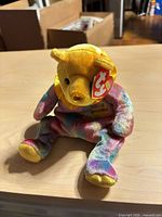 Front view of Ty Beanie Baby plush showing rainbow body, yellow head, gold paws, collar and swing tag