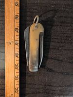 Closed folding knife beside ruler showing 3–4 inch length, bone handle, two folded blades, ring loop