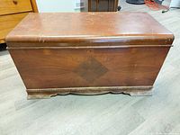 Front and top view of cedar chest showing overall shape, medium-brown finish, diamond veneer pattern, scalloped base