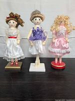 Front view of all three wooden dolls displaying outfits and bases