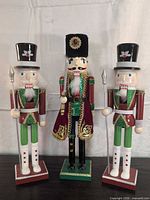Front view of three wooden nutcracker figures with weapons and bases