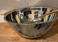 Large stainless steel bowl with gold accent handles and spaghetti fork inside